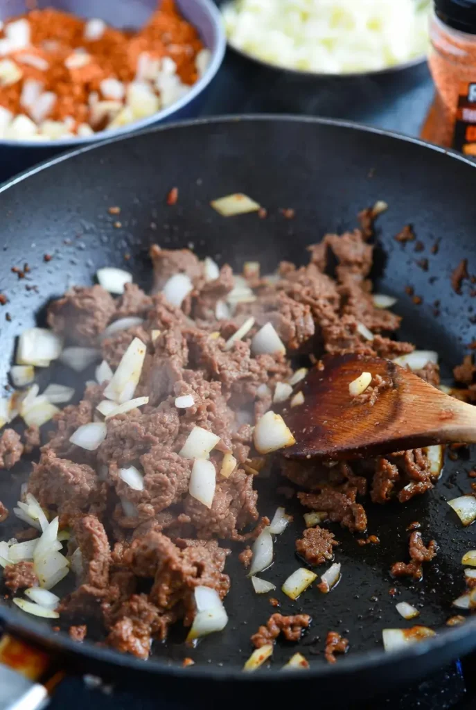 20-Min Prep: Cheesy Taco Stuffed Pasta Shells Recipe 9 ground beef cooking with onions and garlic in a skillet