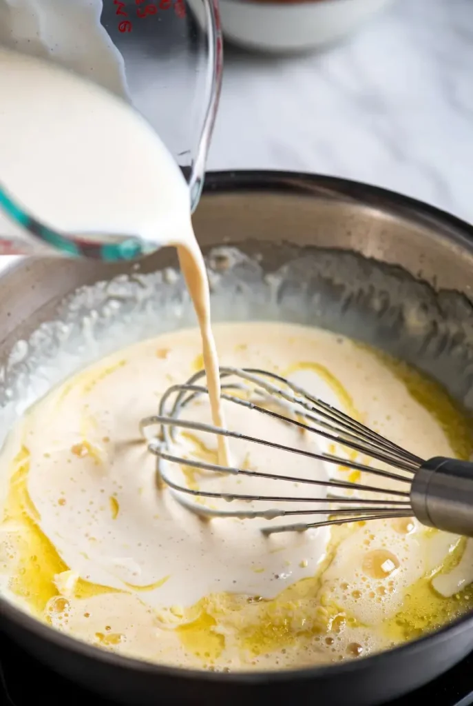 creamy sauce being whisked until smooth in a pan