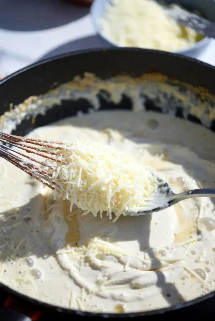 grated parmesan melting into creamy sauce in a pan