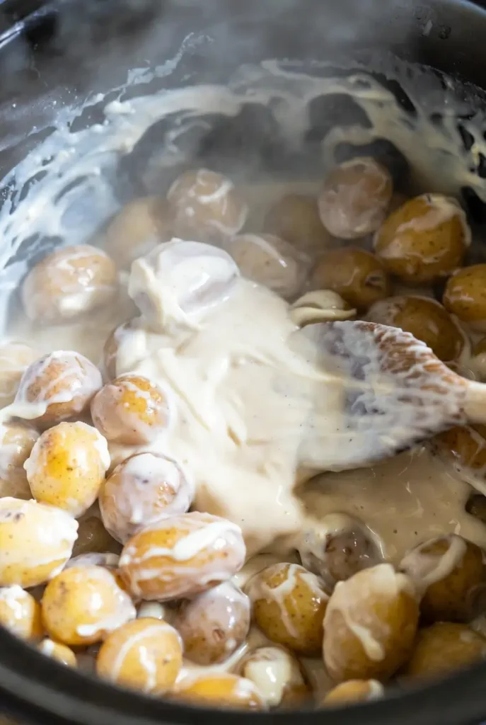 Easy Crockpot Swamp Potatoes (Creamy, Cheesy & Loaded) 11 creamy sauce being poured over potatoes in slow cooker