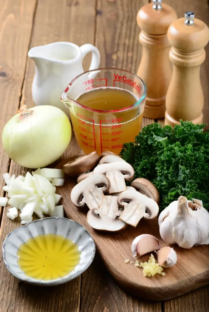 Fresh mushrooms, chopped kale, garlic, onions, cream, and vegetable broth on a kitchen table